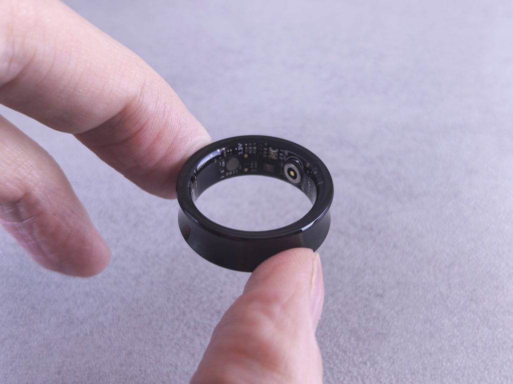 Fingers holding a black smart ring with visible circuitry