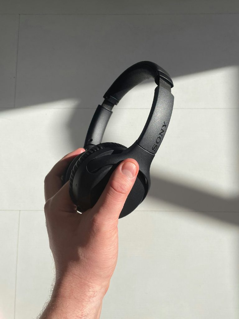 Hand holding a pair of black over-ear headphones against a white wall